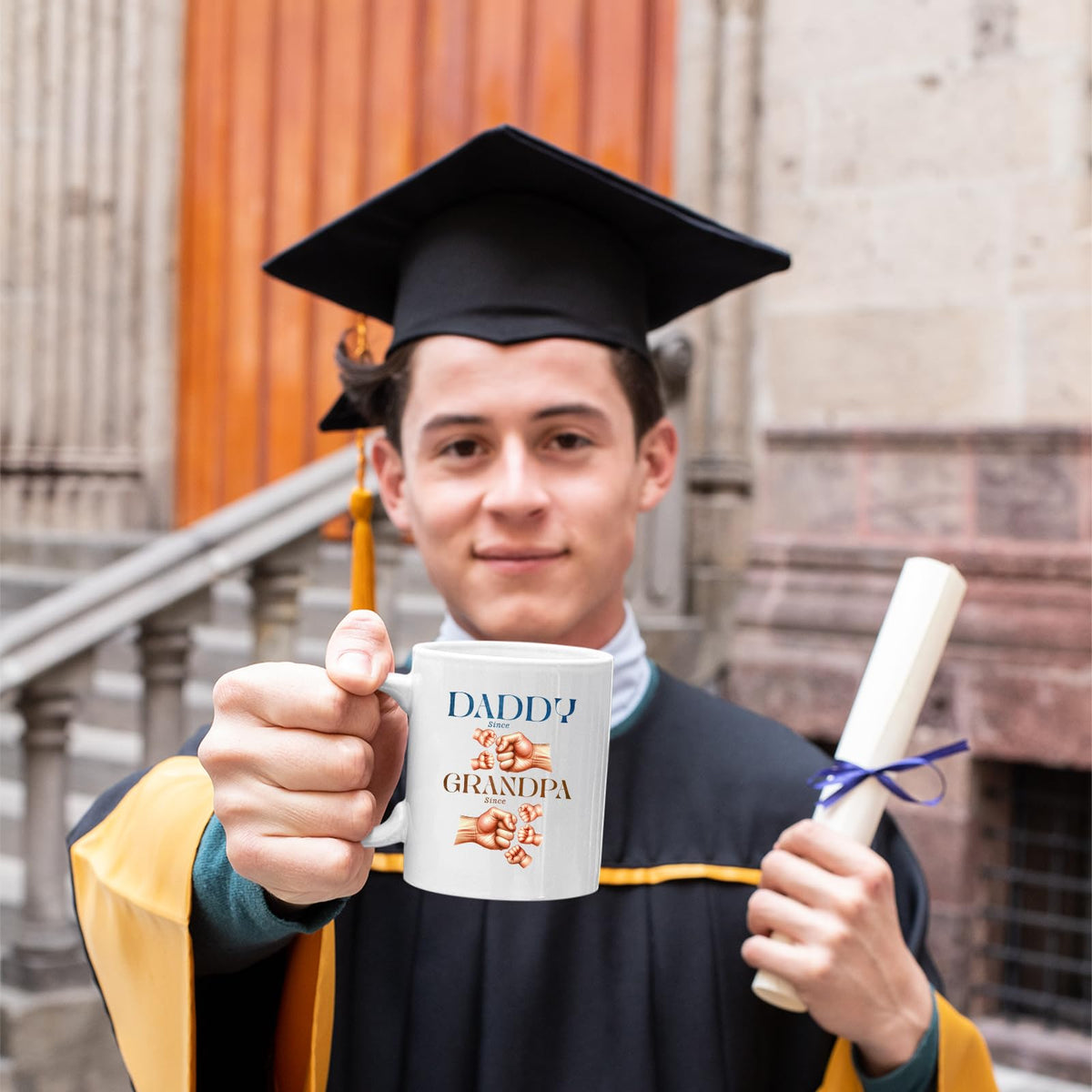 Graduate in cap and gown holding the Daddy and Grandpa fist bump mug