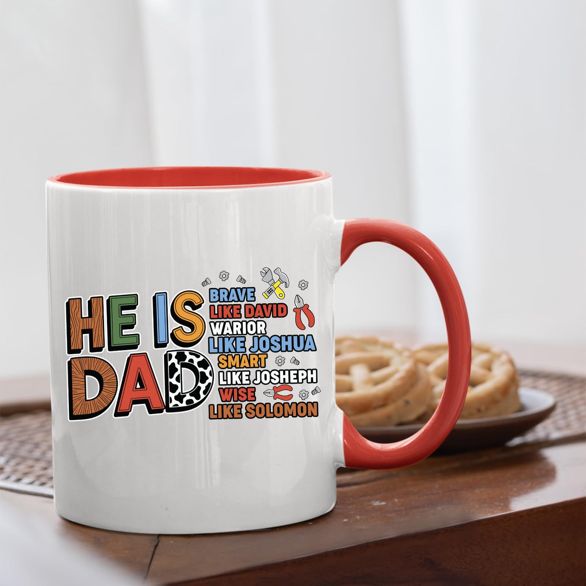Red handle mug with the He Is Dad Bible verse design on a table