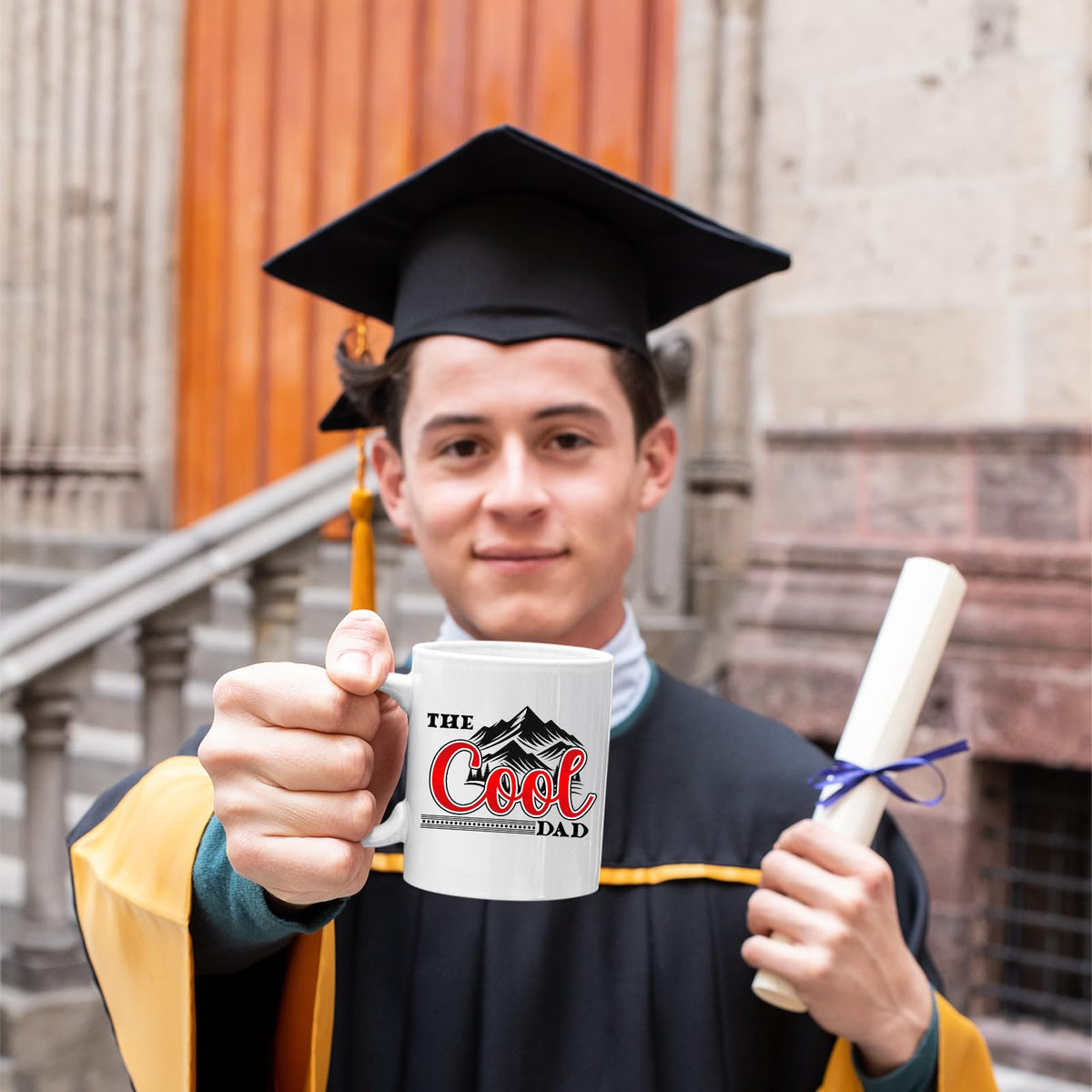 Graduate in cap and gown holding the The Cool Dad mountains mug