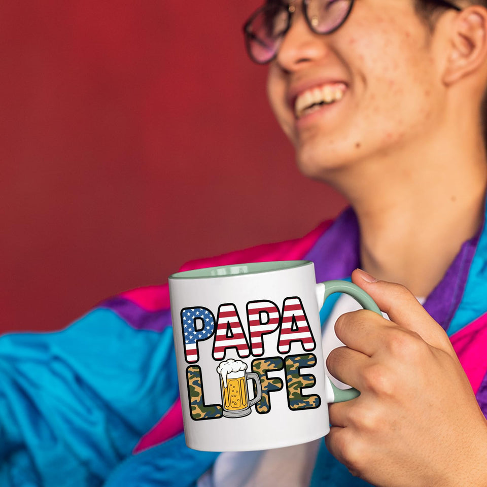 Smiling person in a colourful jacket holding the Papa Life mug with a light green handle