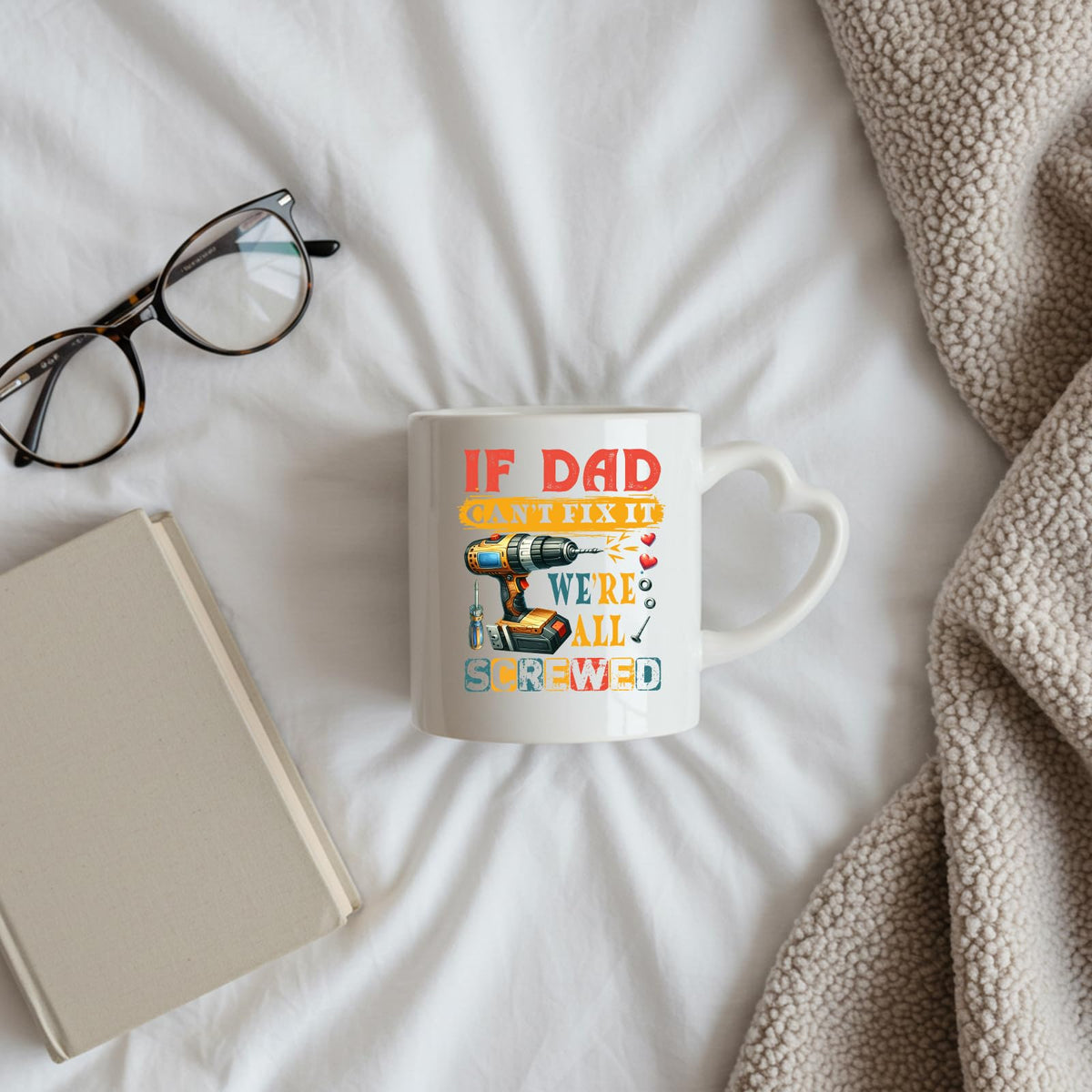 If Dad Can’t Fix It heart-handle mug on a bed beside glasses and a book