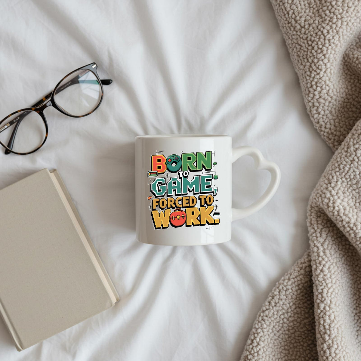 Born to Game heart-handle mug on a bed beside glasses and a book