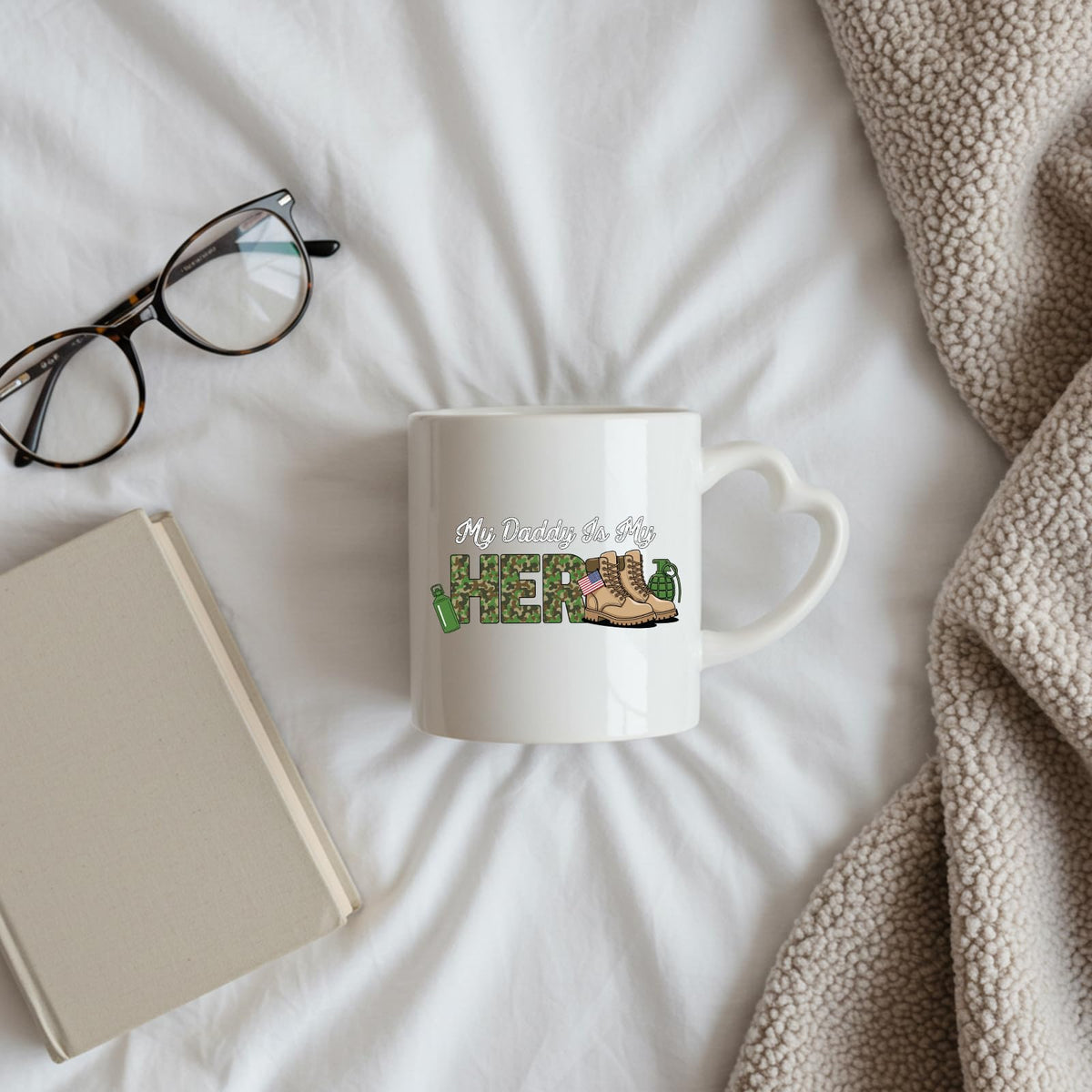 My Daddy Is My Hero military heart-handle mug on a bed beside glasses and a book