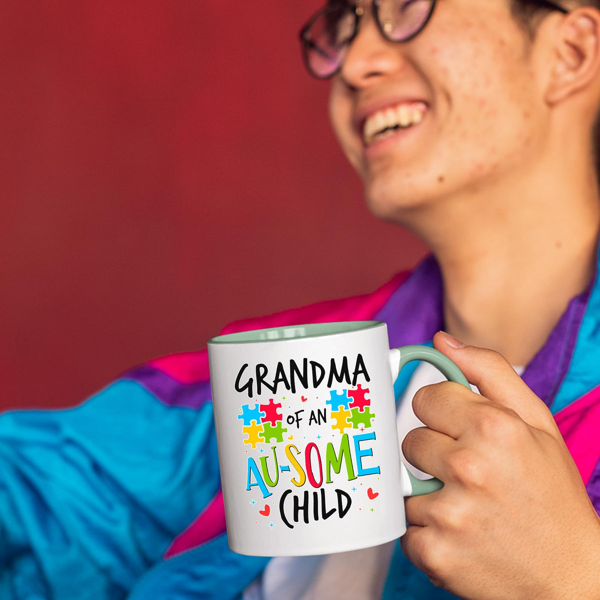 Smiling person in a colourful jacket holding the Grandma of an Au-Some Child mug with a light green handle