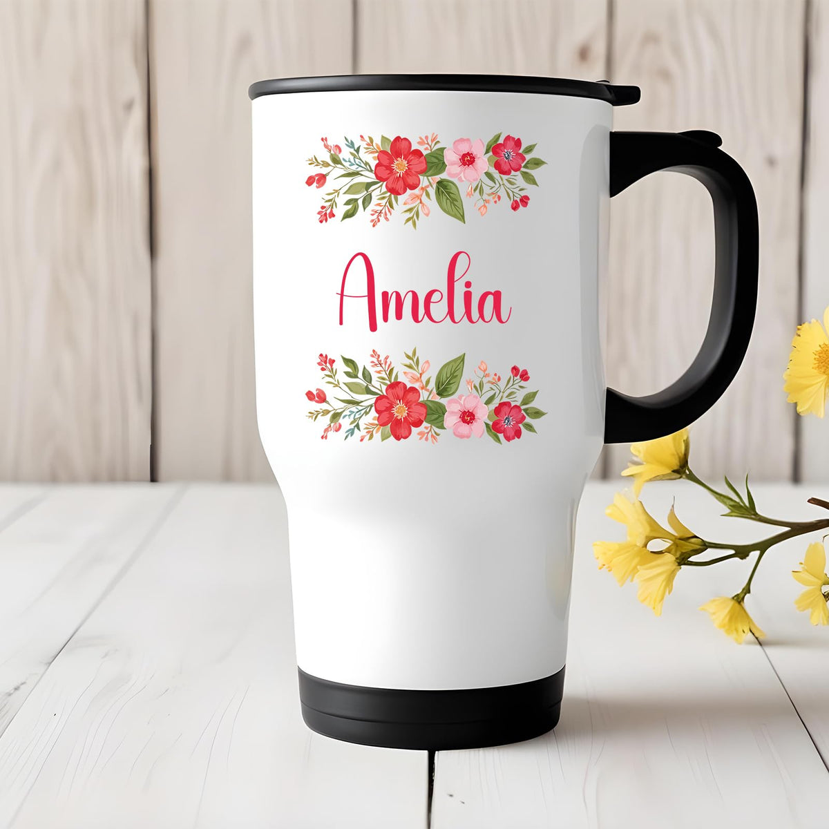 Travel mug with a red flower border around an example name on a white table with yellow flowers