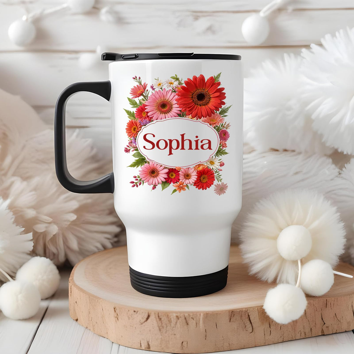 Travel mug with a red gerbera wreath around an example name on a wooden board with white pompoms
