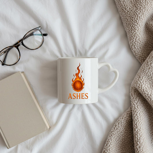 Ashes heart-handle mug on a bed beside glasses and a notebook
