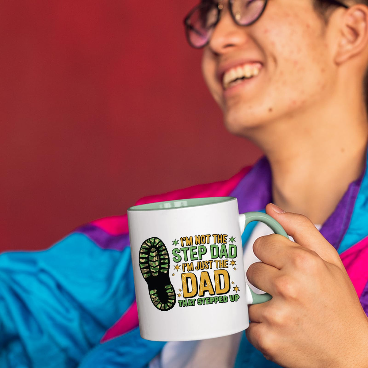Smiling person in a colourful jacket holding the Dad That Stepped Up mug with a light green handle