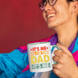 Smiling person in a colourful jacket holding the It’s Me Hi I’m the Dad mug with a light green handle
