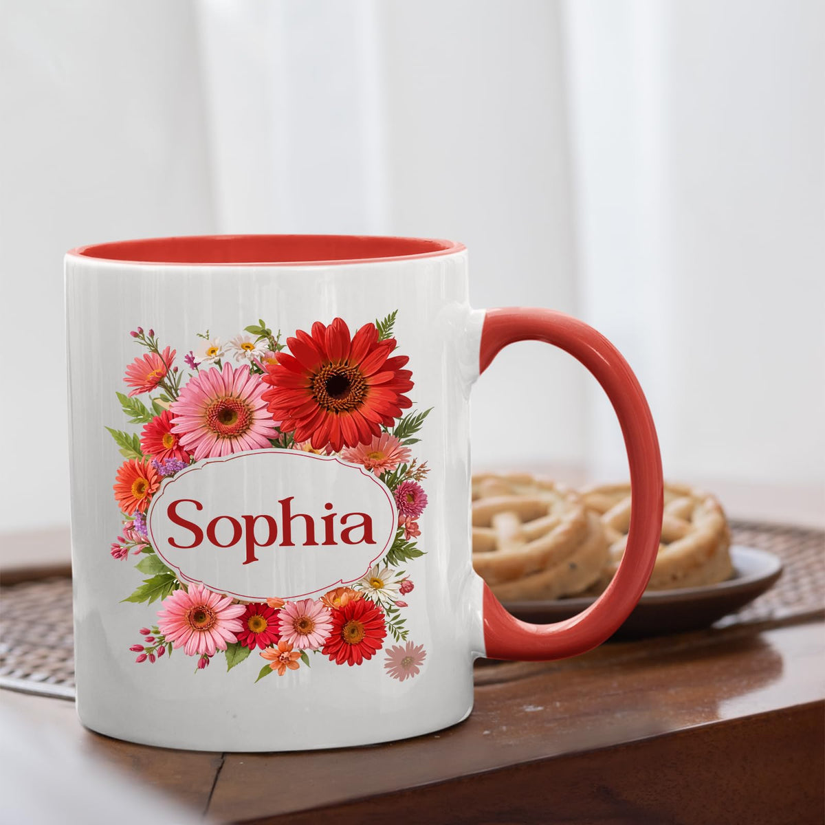 Red handle mug with a red gerbera wreath around an example name on a table