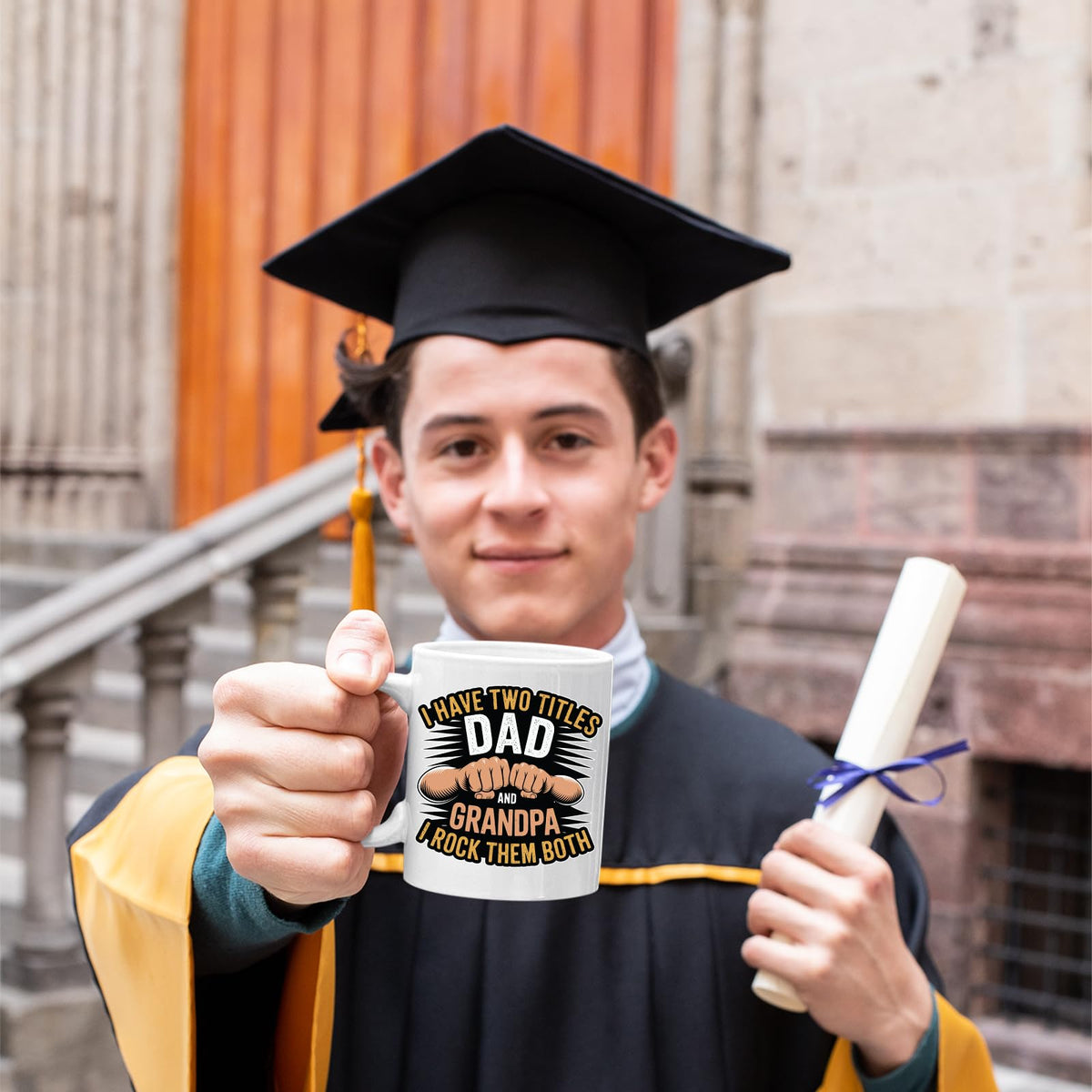 Graduate in cap and gown holding the Two Titles Dad and Grandpa mug