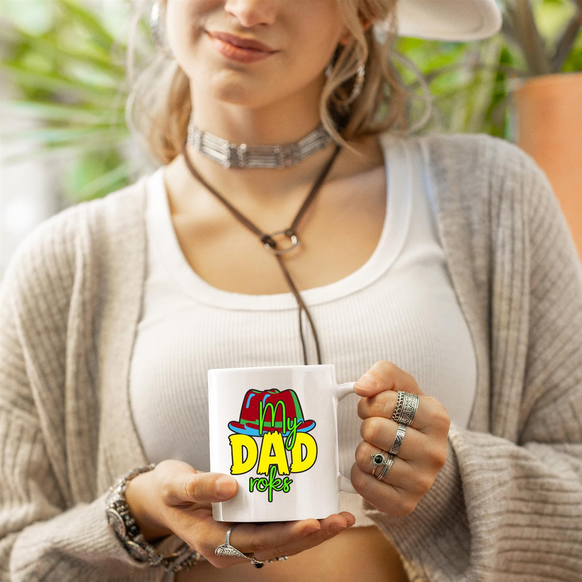 Woman in a cardigan holding a white mug with the colourful My Dad Rocks hat design