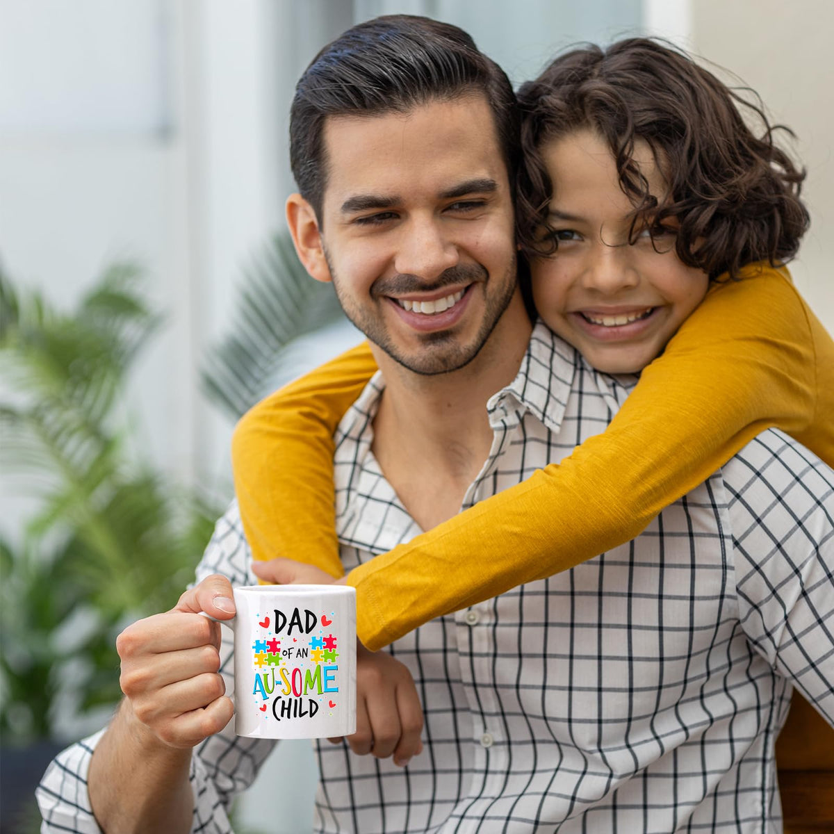 Smiling dad holding the Dad of an Au-Some Child mug as his son hugs him