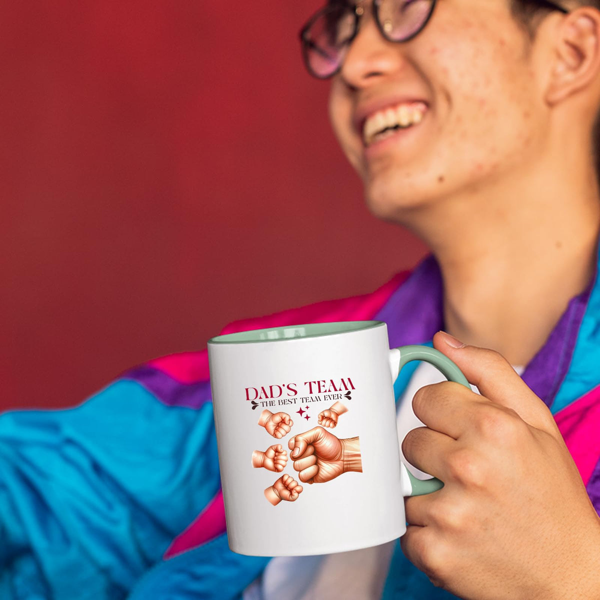 Smiling person in a colourful jacket holding the Dad’s Team fist bump mug with a light green handle