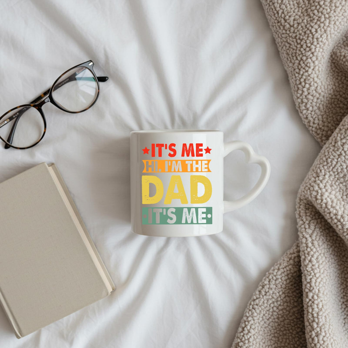 It’s Me Hi I’m the Dad heart-handle mug on a bed beside glasses and a book