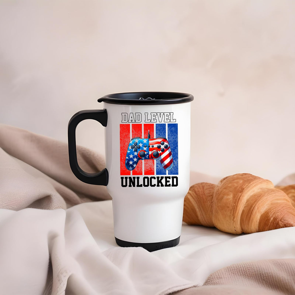 Dad Level Unlocked travel mug on a soft blanket beside a croissant