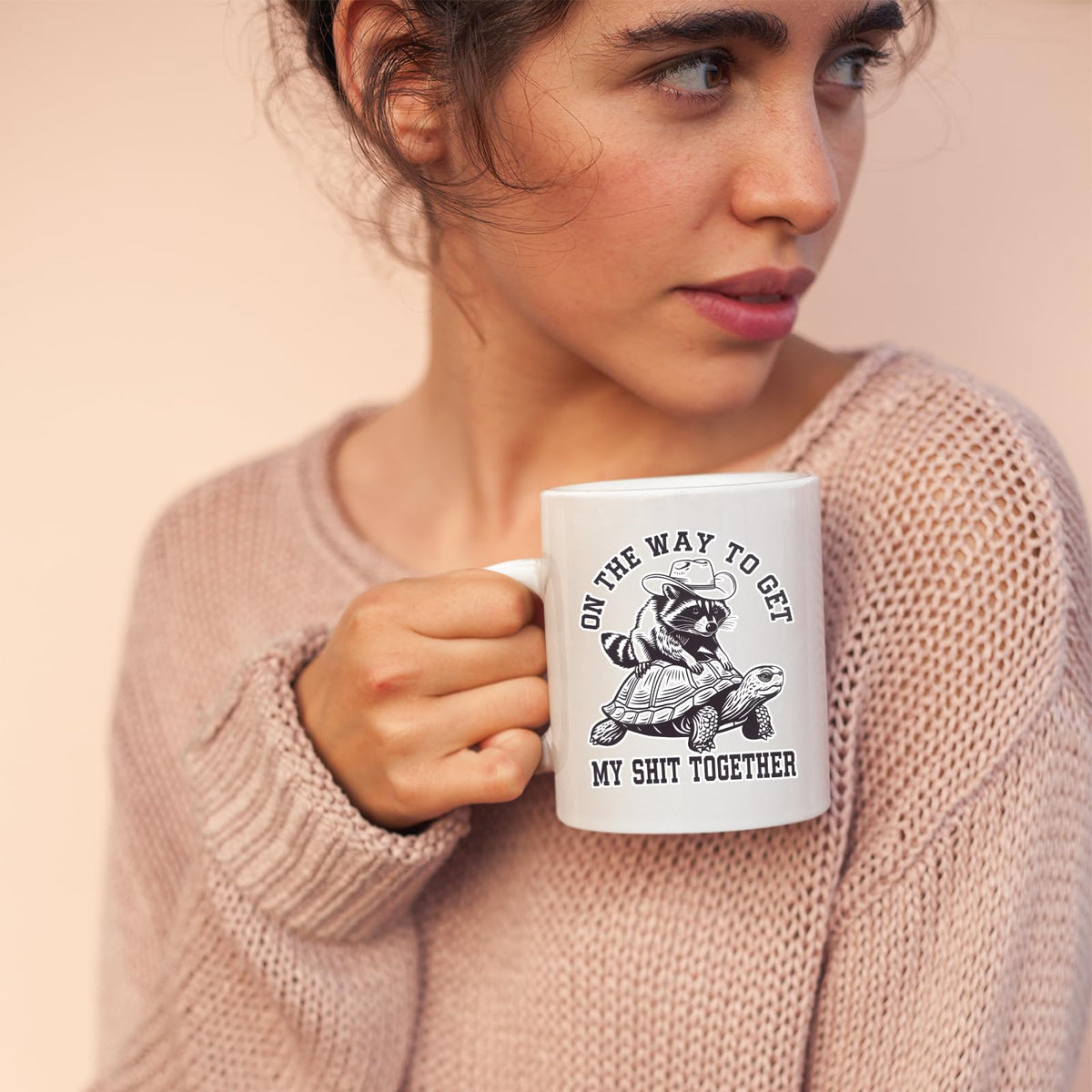 Woman in a pink jumper holding the raccoon and tortoise mug