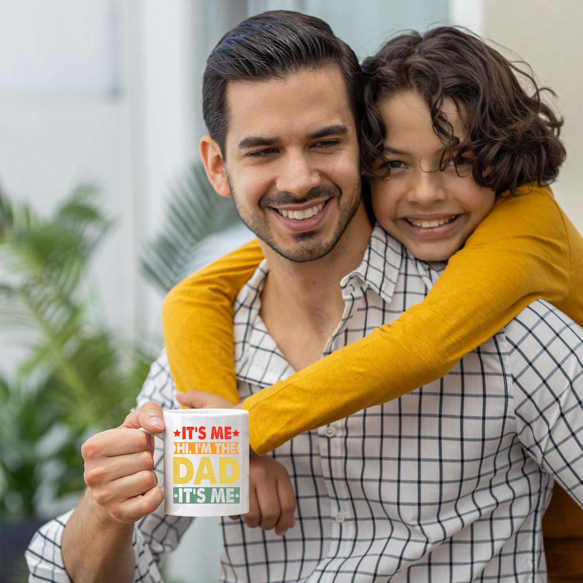 Smiling dad holding the It’s Me Hi I’m the Dad mug as his son hugs him