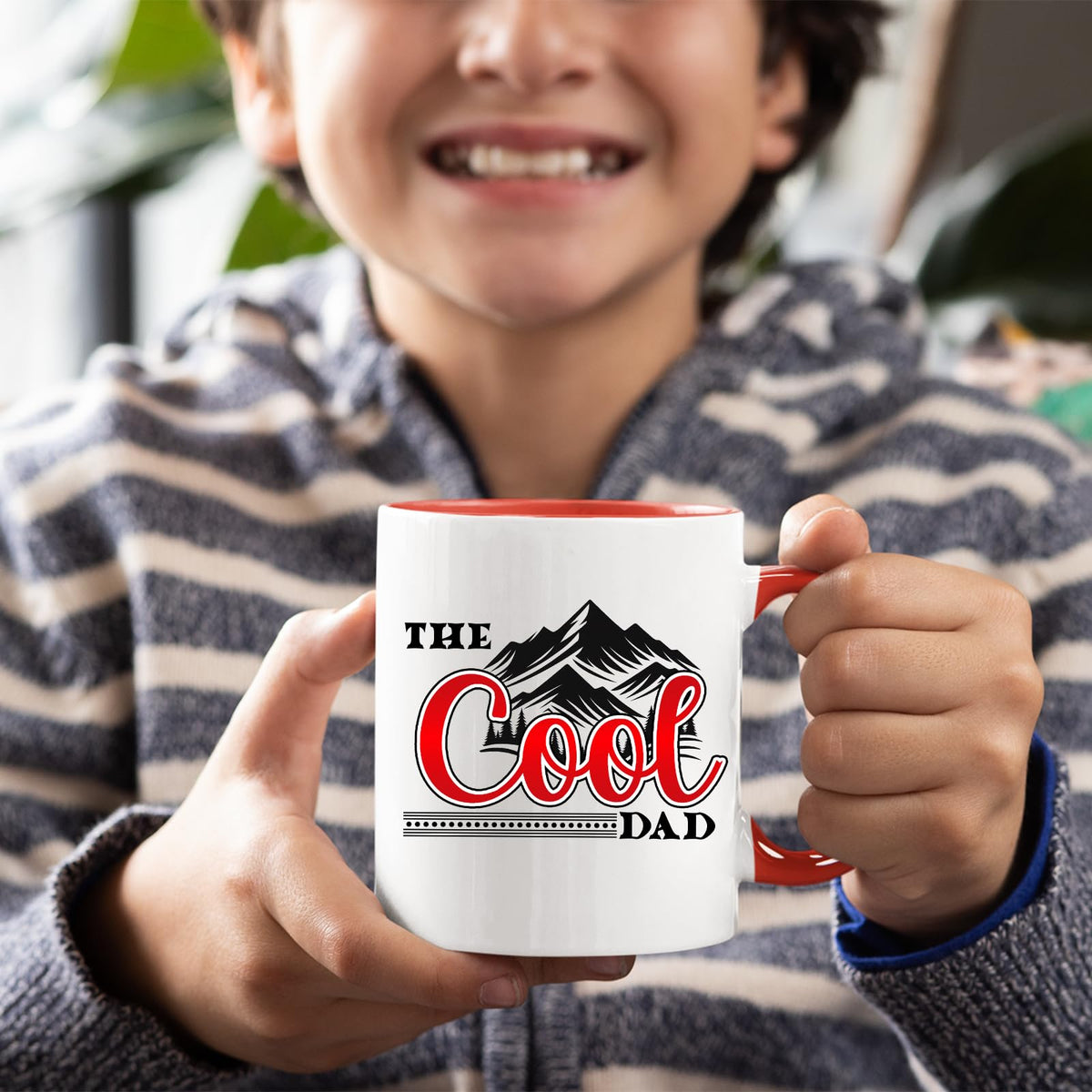 Smiling child holding the The Cool Dad mountains mug with a red handle