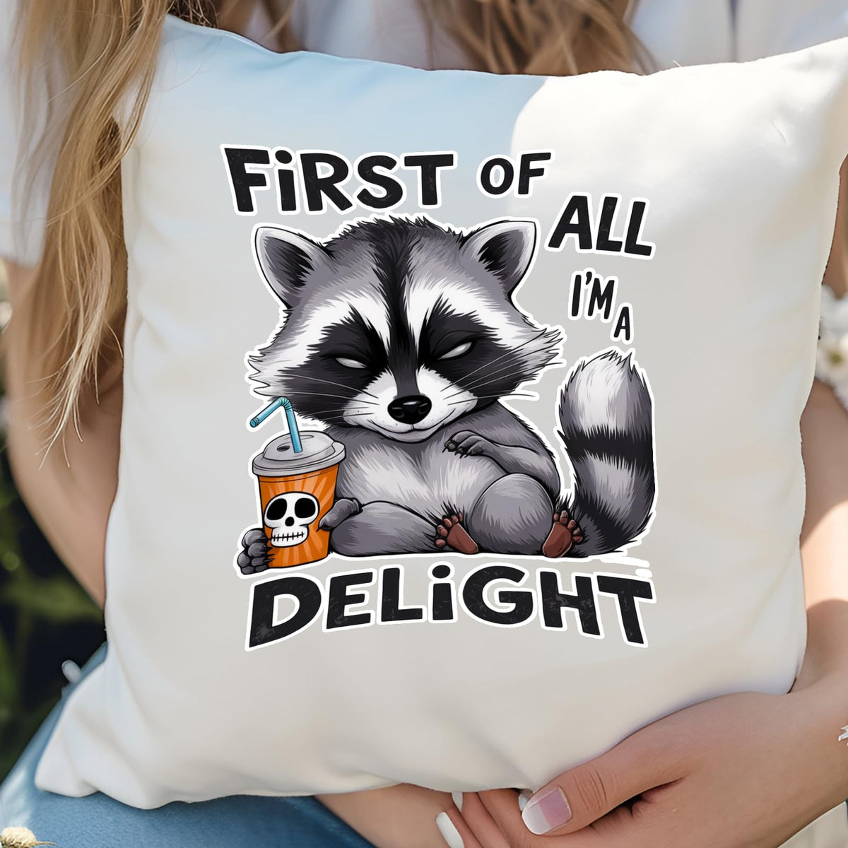 Hands holding the First of All I’m a Delight raccoon cushion