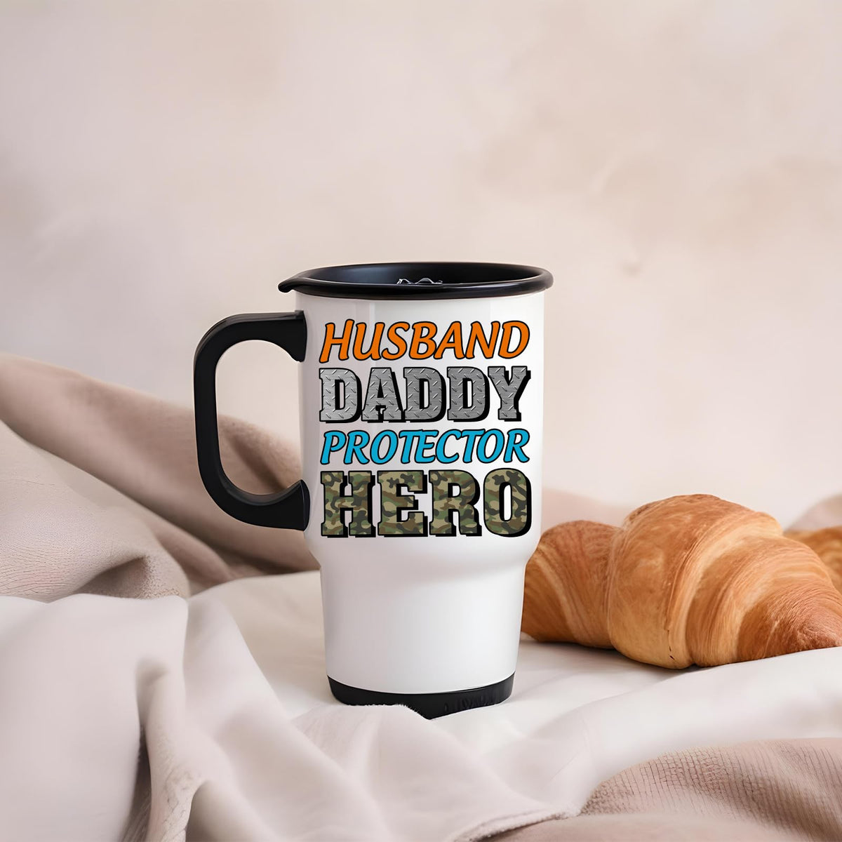 Husband Daddy Protector Hero camo travel mug on a soft blanket beside a croissant