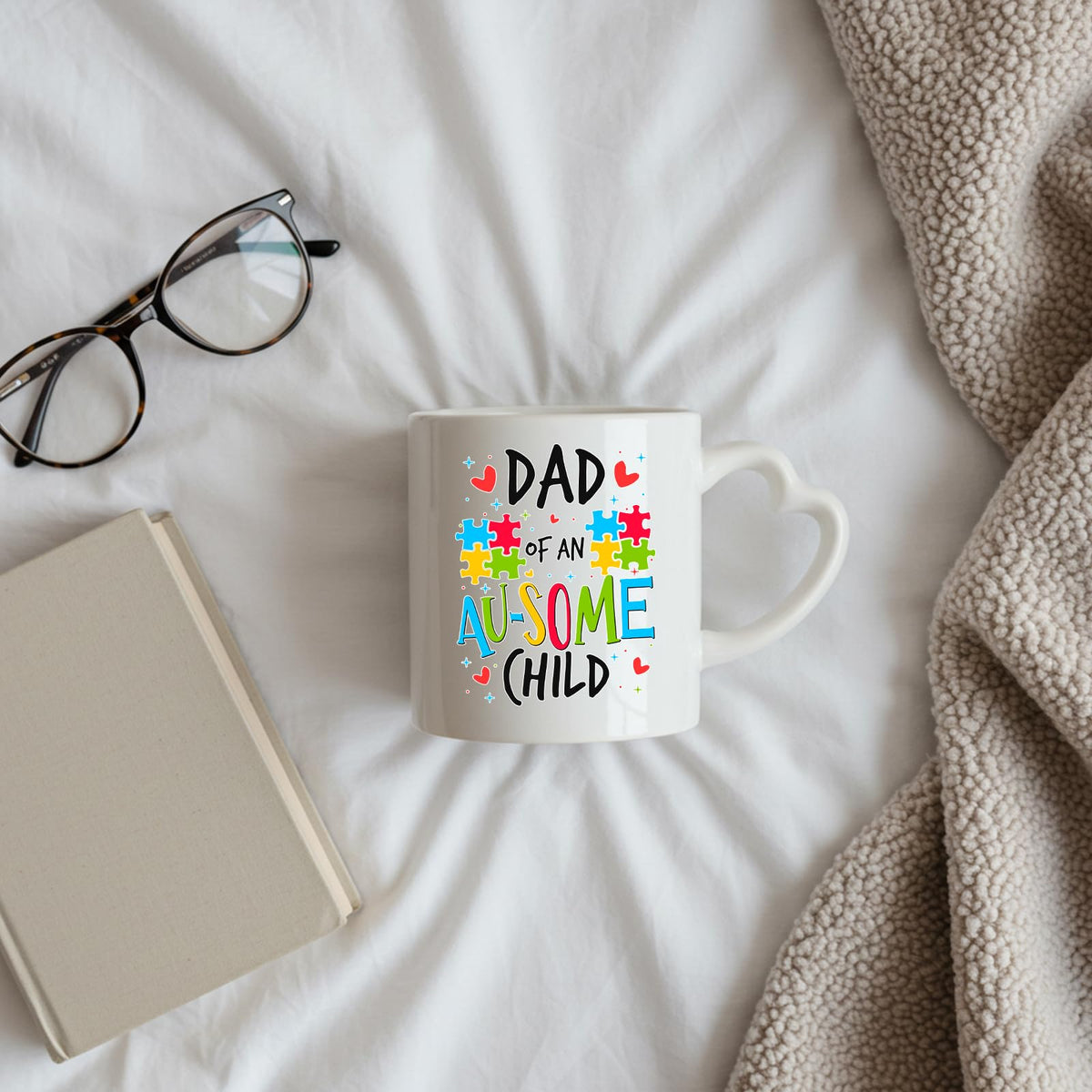Dad of an Au-Some Child heart-handle mug on a bed beside glasses and a book