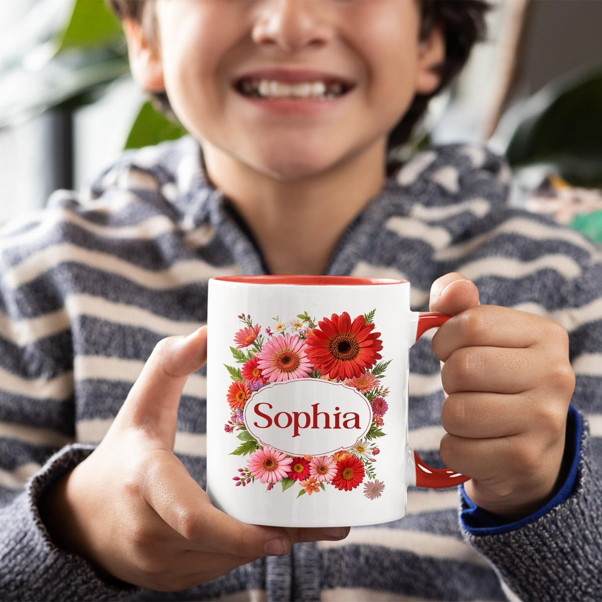 Boy holding a red handle mug with a red gerbera wreath around an example name
