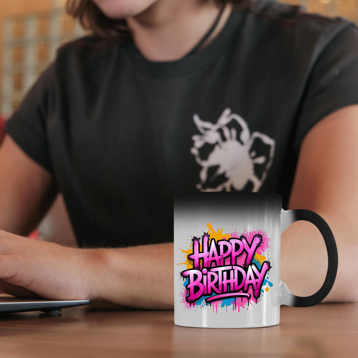 Happy Birthday pink graffiti splash colour changing mug on a desk beside a laptop
