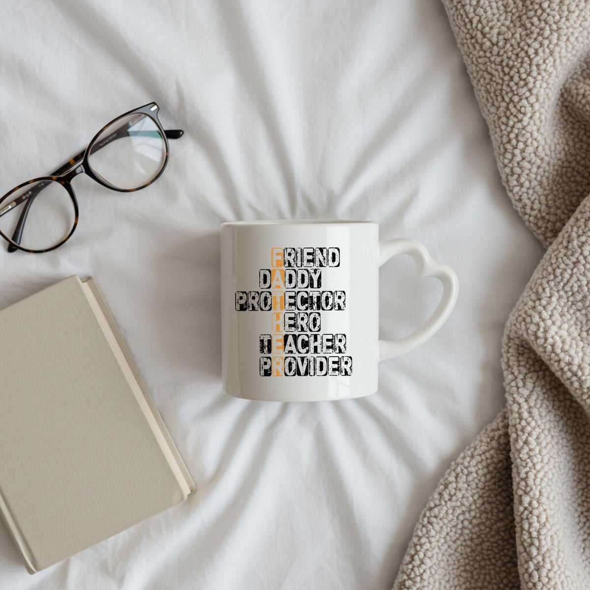 FATHER acrostic heart-handle mug on a bed beside glasses and a book