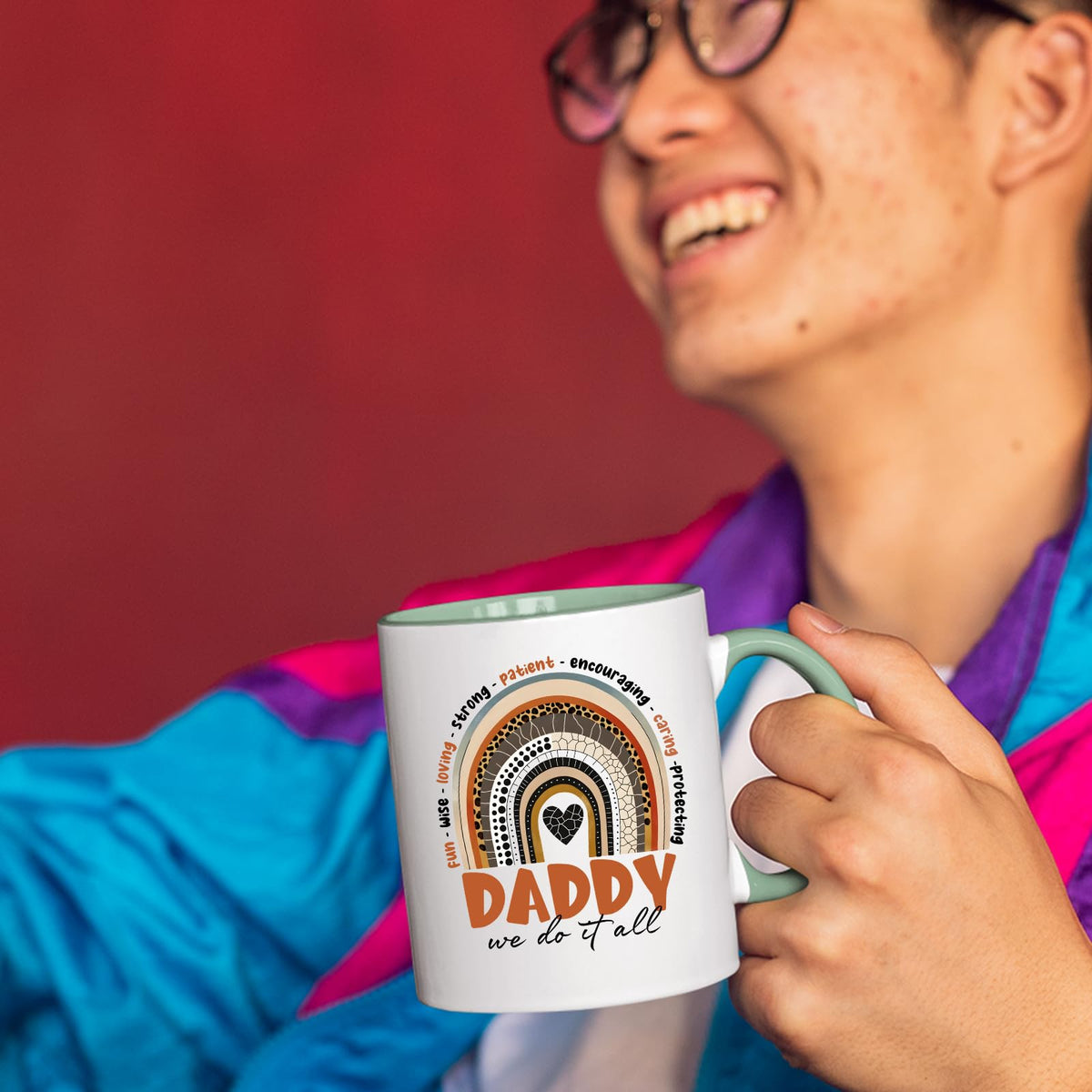 Smiling person in a colourful jacket holding the Daddy boho rainbow mug with a light green handle