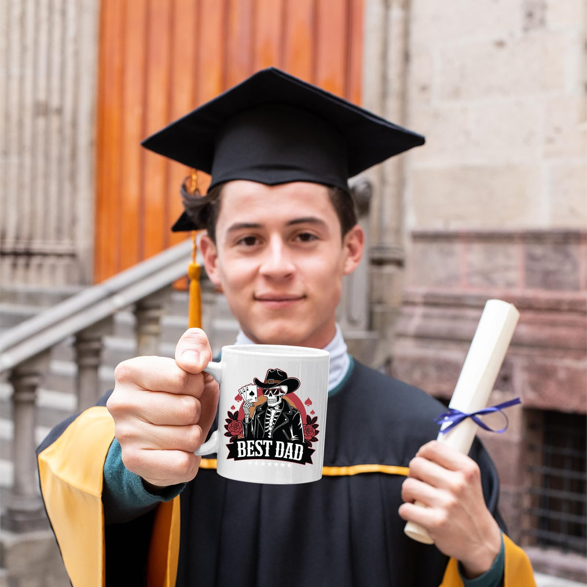 Graduate in cap and gown holding the Best Dad skeleton cowboy mug