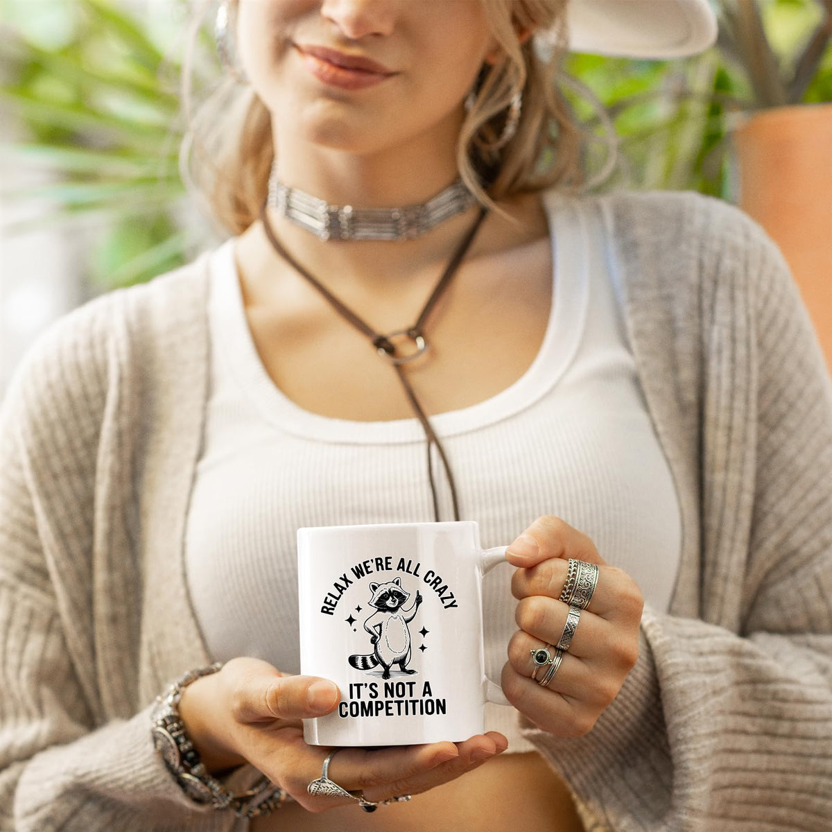 Woman in a cardigan holding the Relax We’re All Crazy raccoon mug