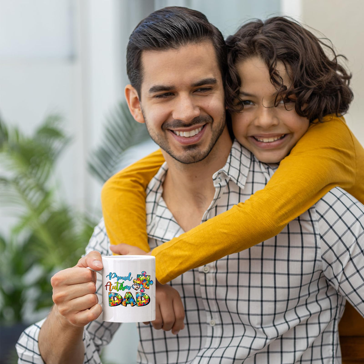 Smiling dad holding the Proud Autism Dad mug as his son hugs him