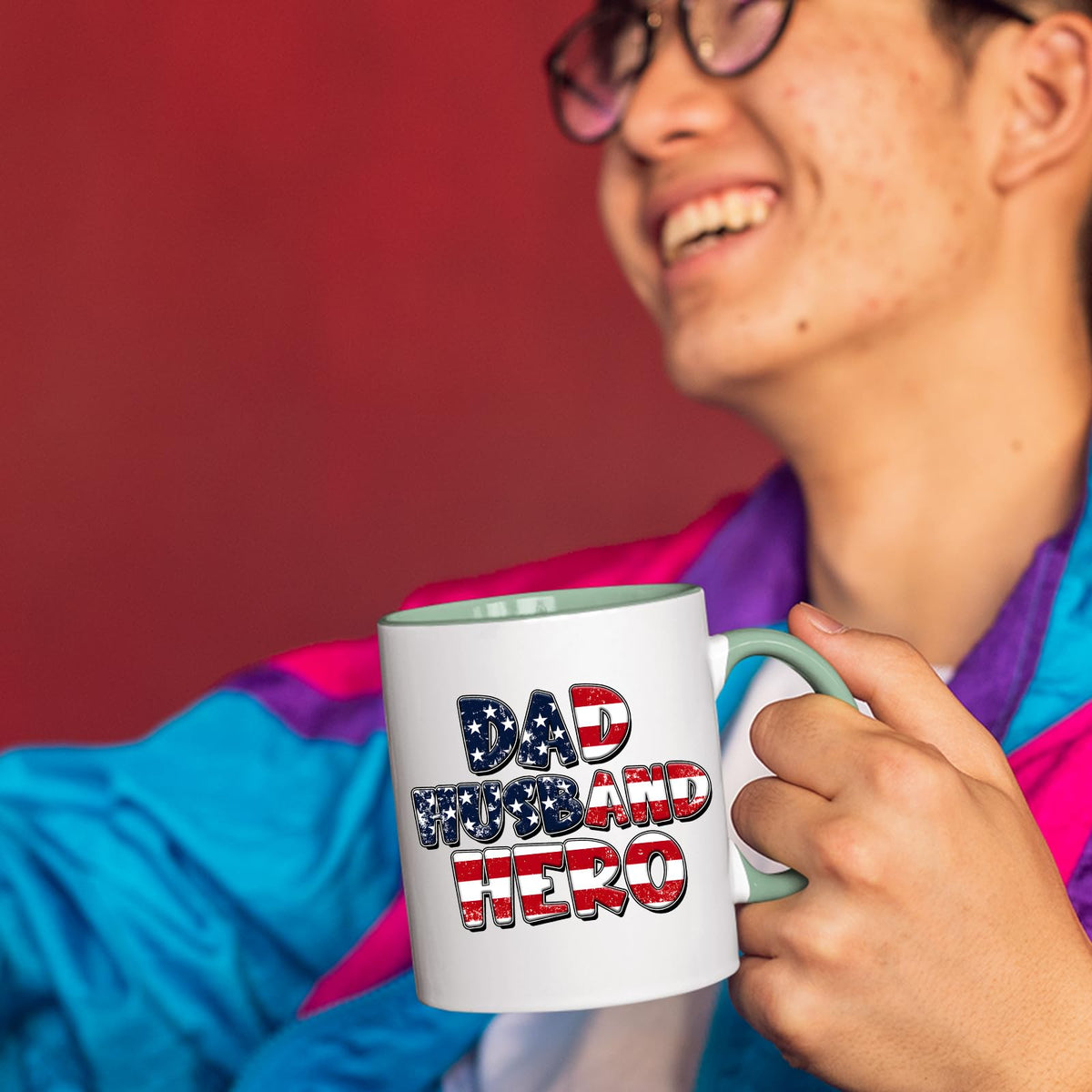Smiling person in a colourful jacket holding the Dad Husband Hero mug with a light green handle