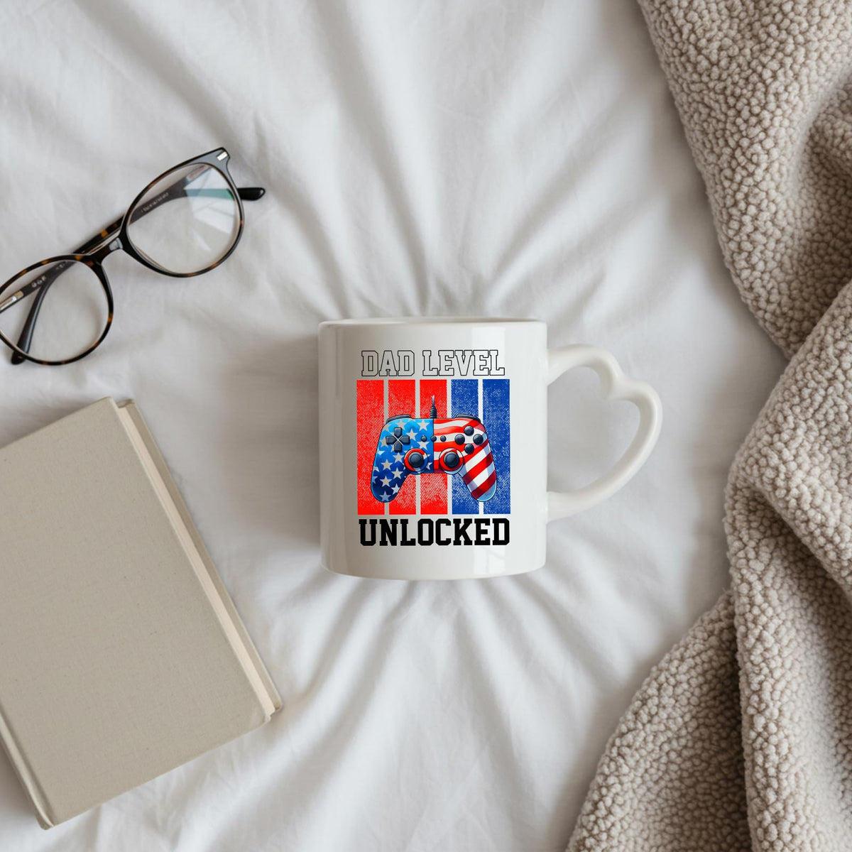 Dad Level Unlocked heart-handle mug on a bed beside glasses and a book