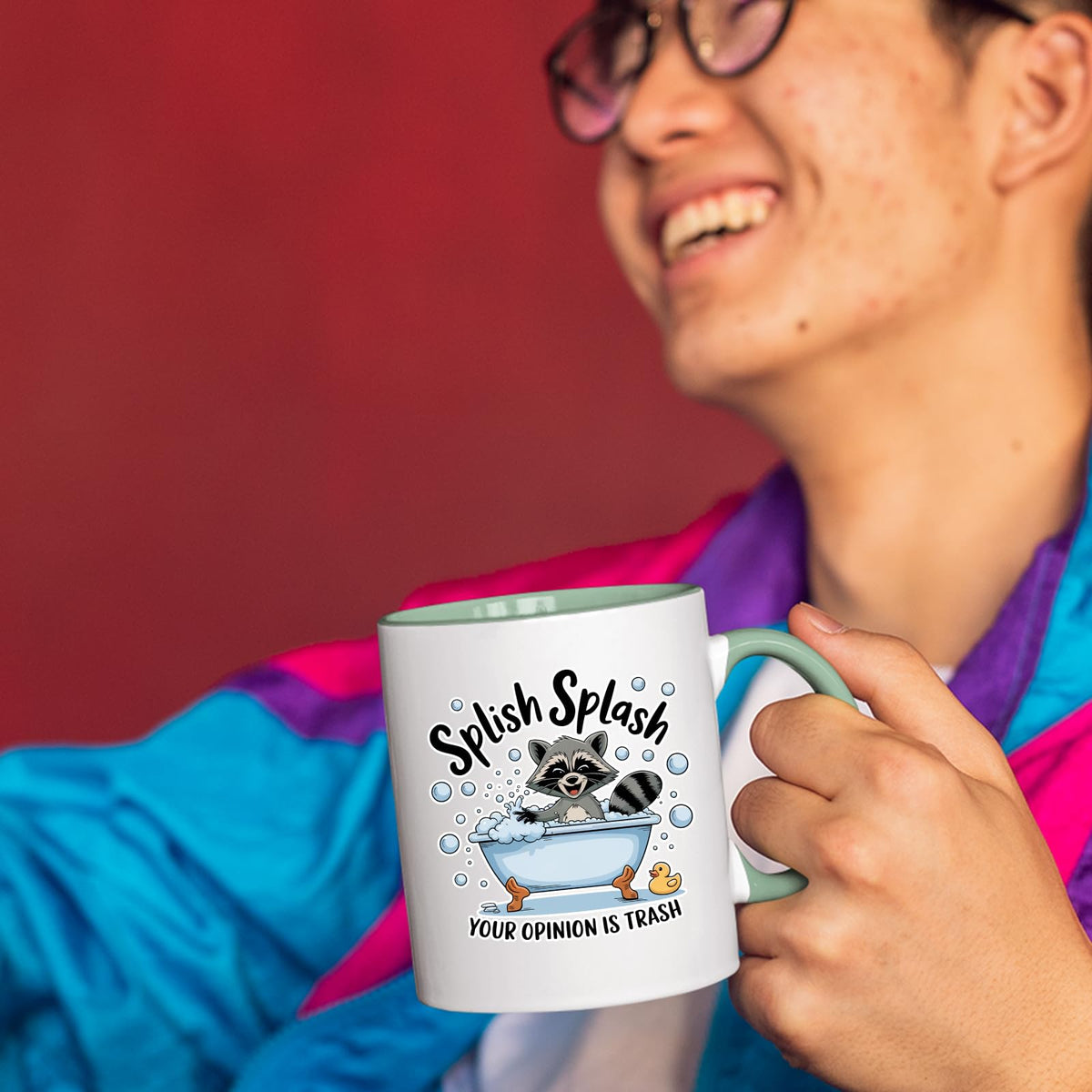 Smiling person in a colourful jacket holding the Splish Splash raccoon mug with a light green handle