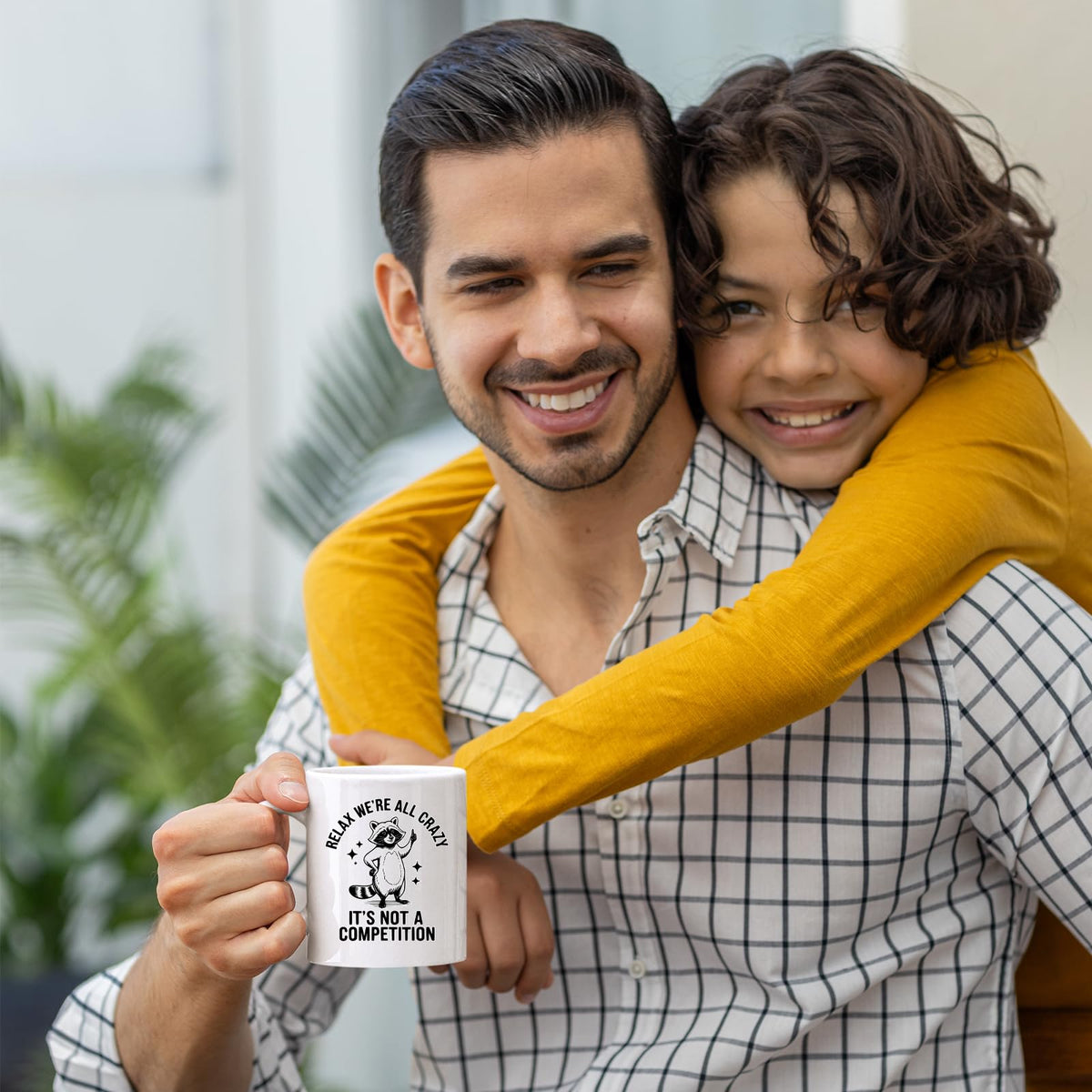 Smiling dad holding the Relax We’re All Crazy raccoon mug as his son hugs him