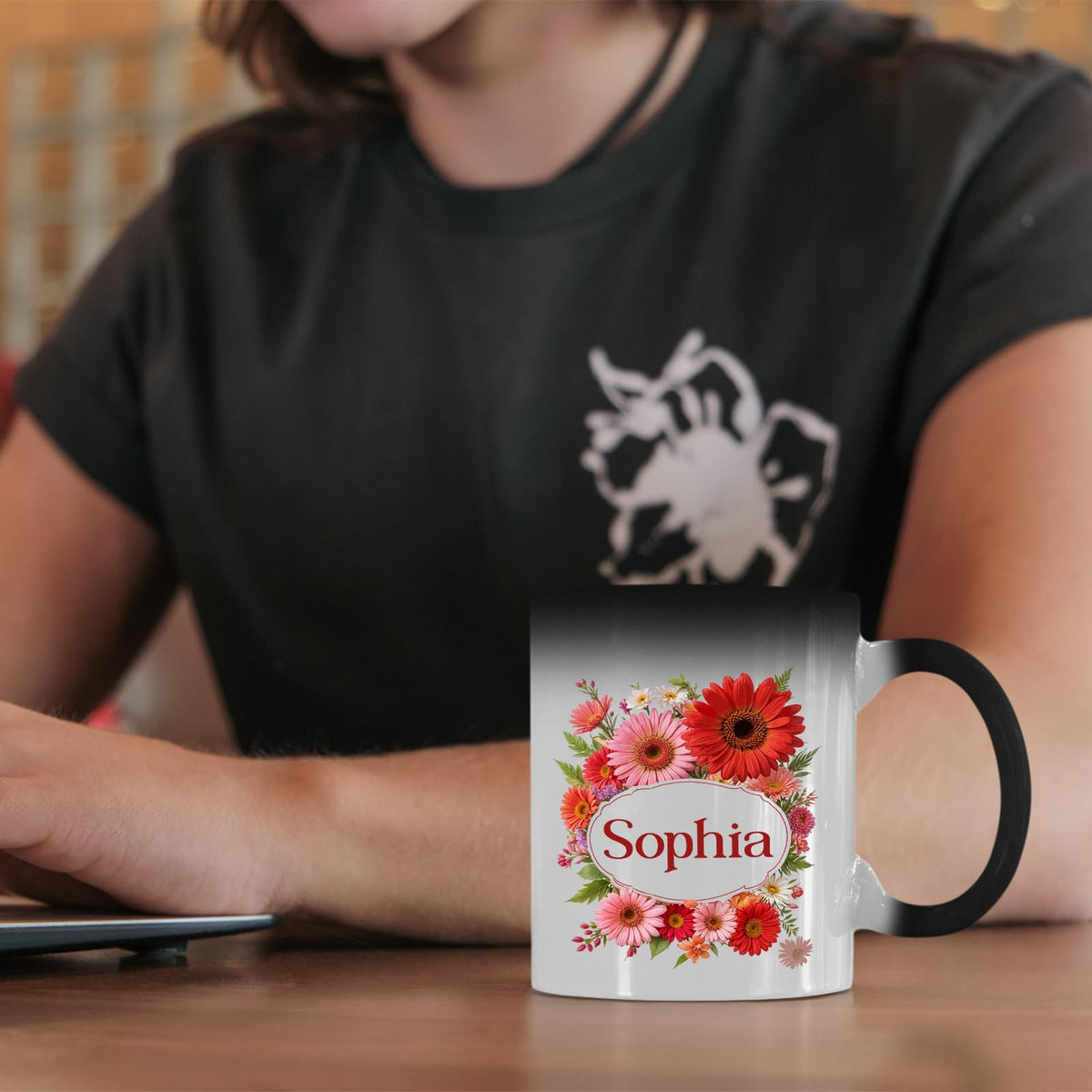 Colour changing mug with a red gerbera wreath around an example name on a desk