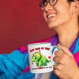 Smiling person in a colourful jacket holding the Triceratops dad mug with a light green handle