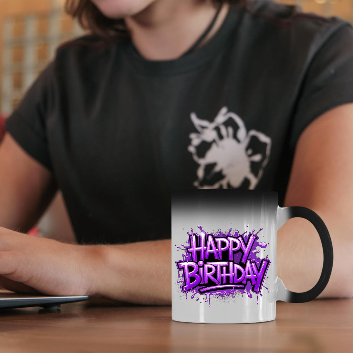 Happy Birthday purple graffiti colour changing mug on a desk beside a laptop