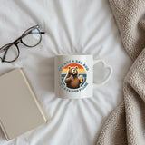 Dad Bod bear heart-handle mug on a bed beside glasses and a book