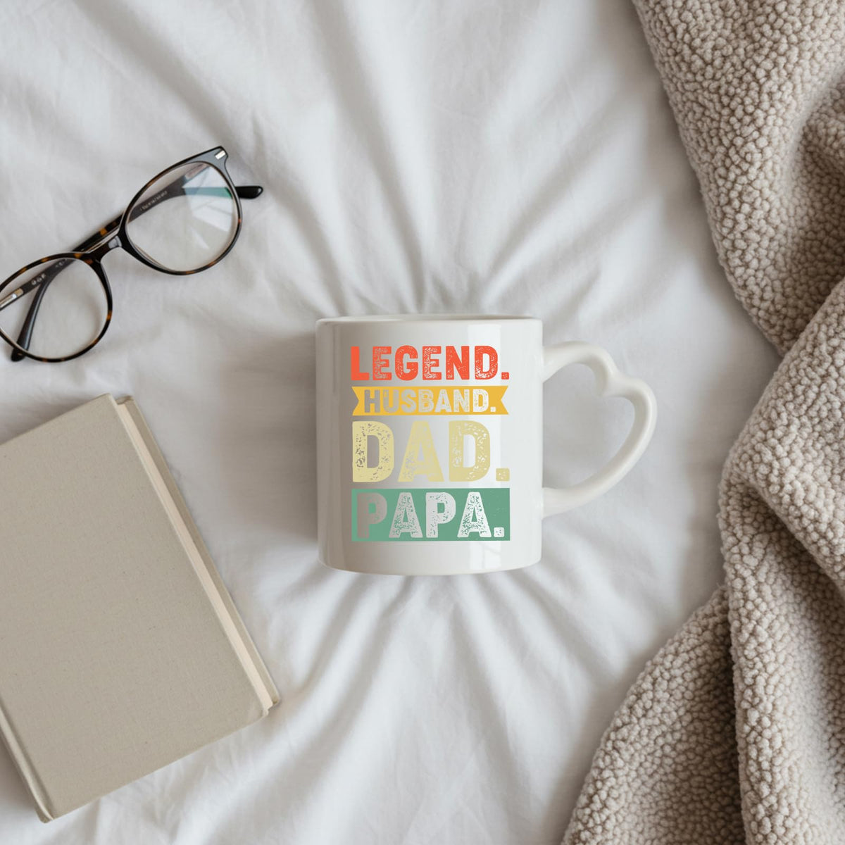 Legend Husband Dad Papa heart-handle mug on a bed beside glasses and a book