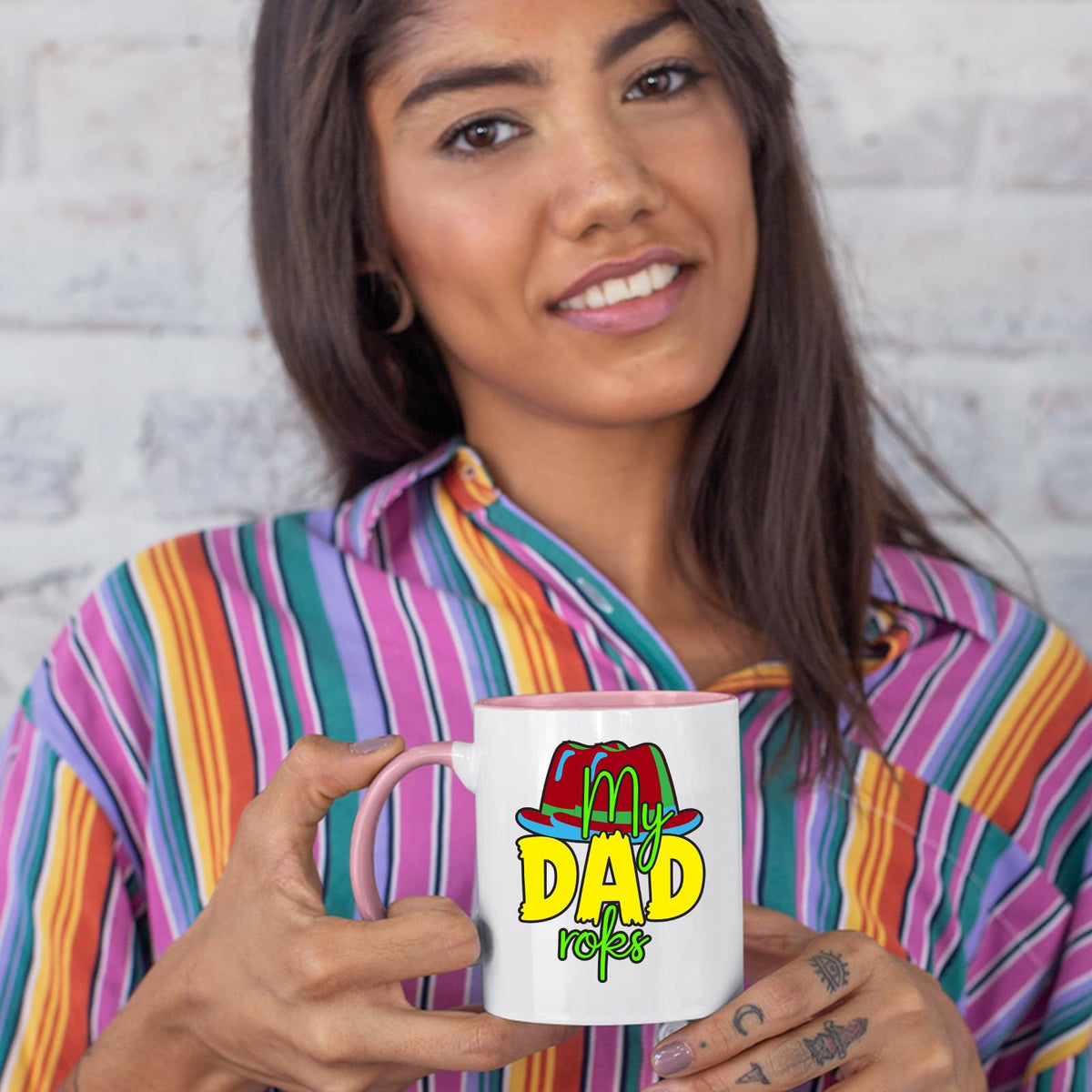 Woman in a striped shirt holding a colour handle mug with the colourful My Dad Rocks hat design