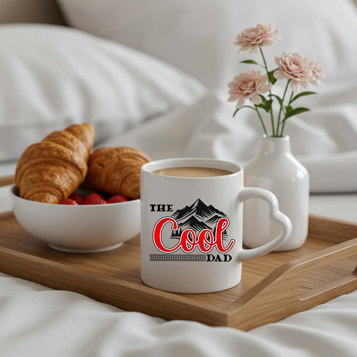 The Cool Dad mountains heart-handle mug on a breakfast tray with croissants and flowers
