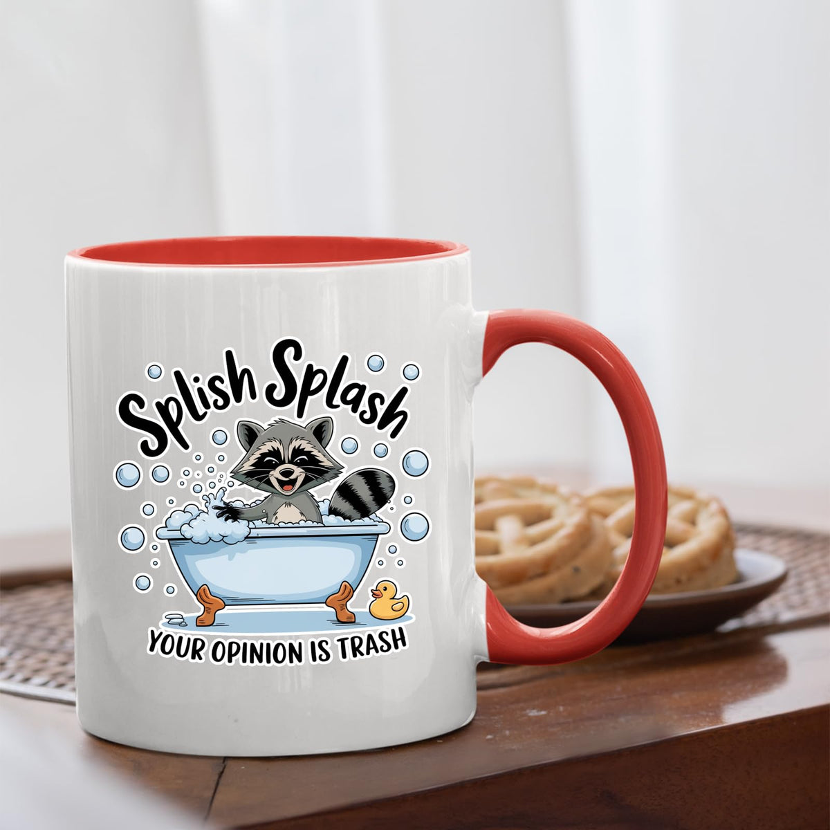 Splish Splash raccoon mug with a red handle beside biscuits