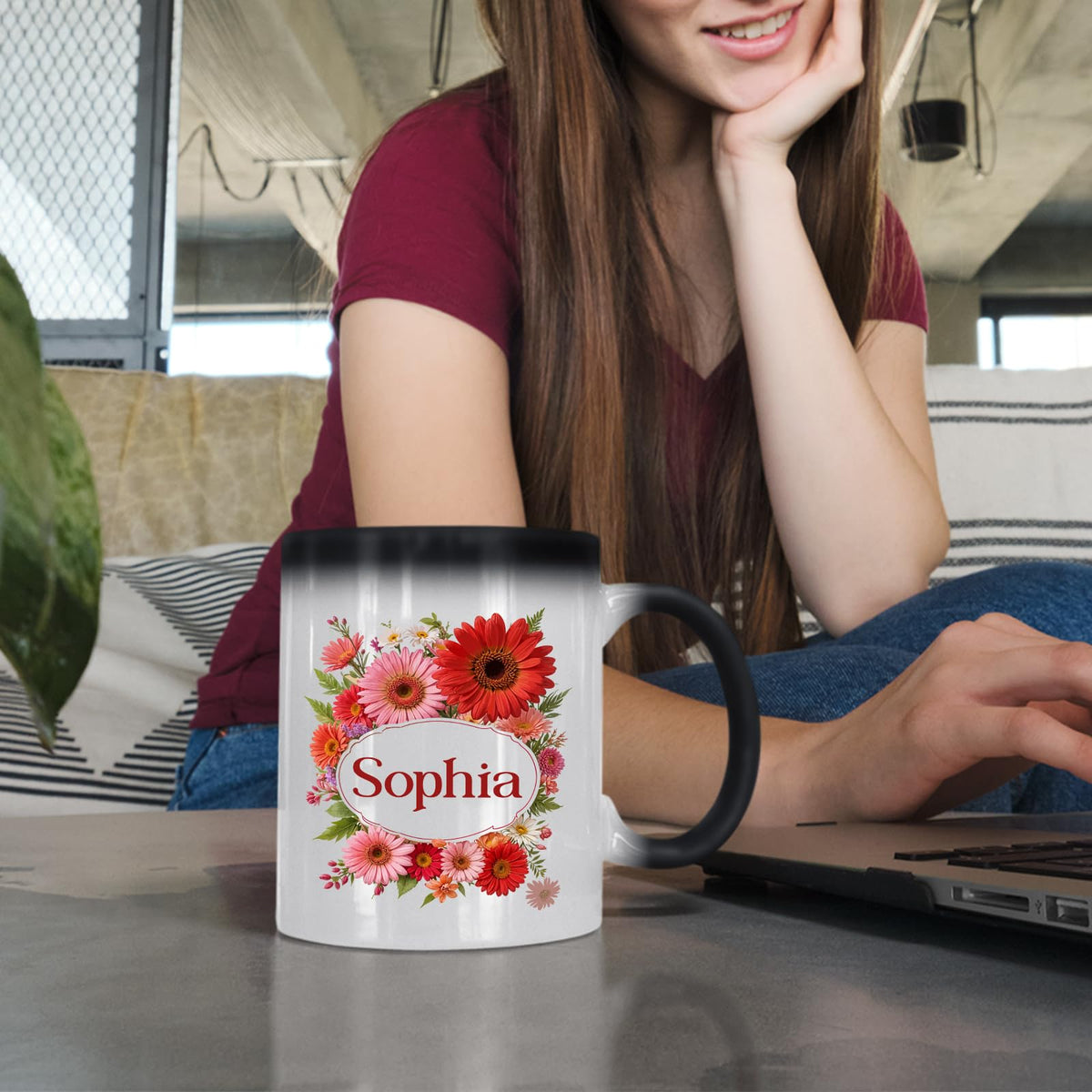 Woman at a laptop with a colour changing mug showing a red gerbera wreath around an example name