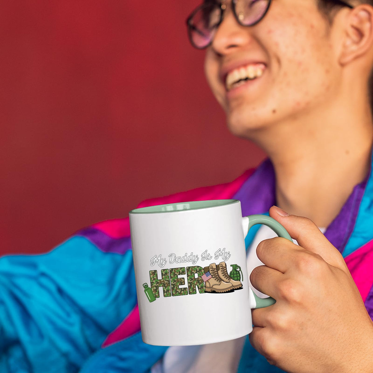 Smiling person in a colourful jacket holding the My Daddy Is My Hero military mug with a light green handle