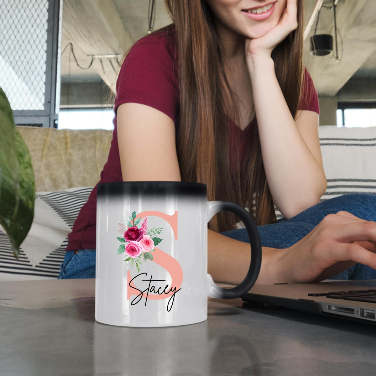 Woman at a laptop with a colour changing mug showing a blush pink initial with roses and an example name