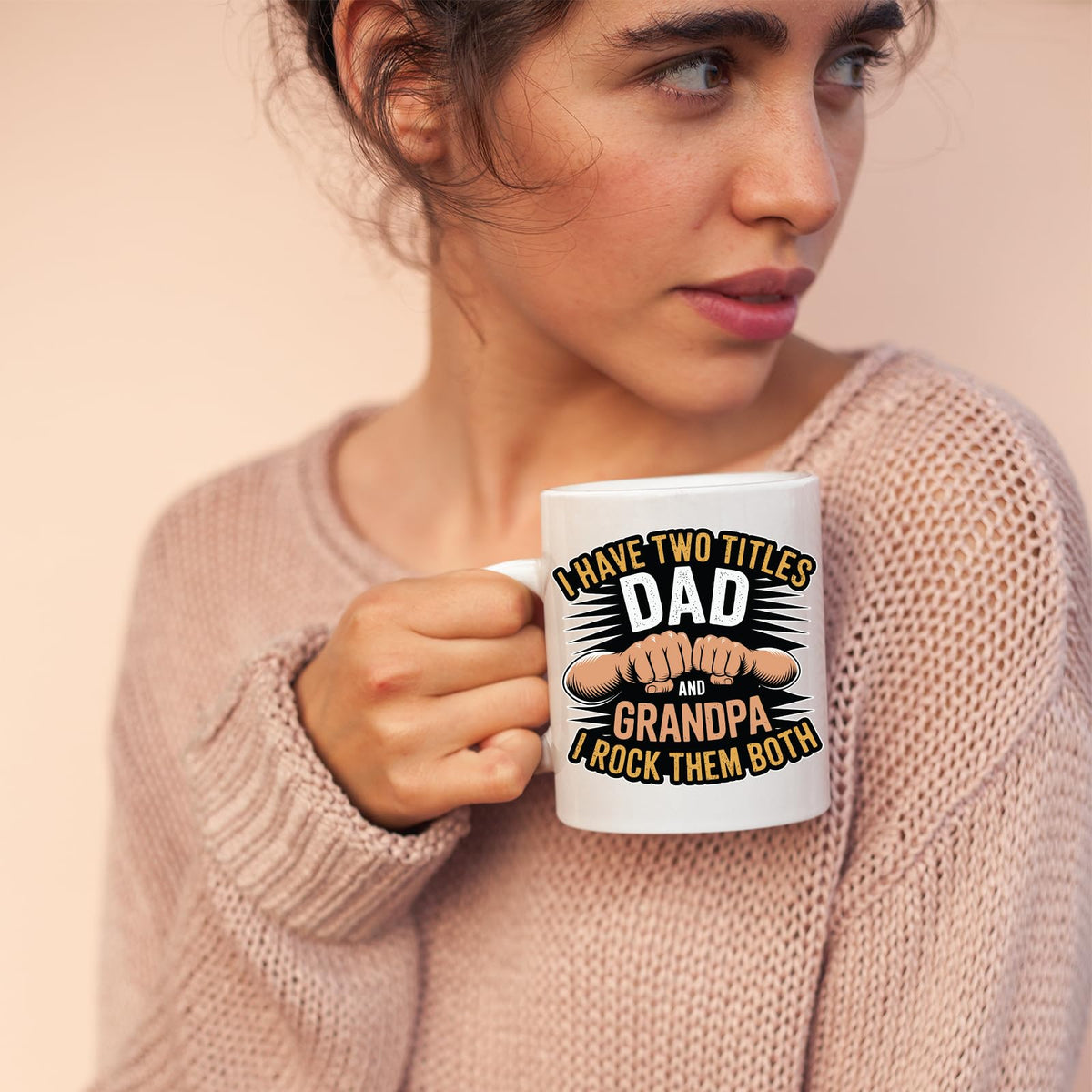 Woman in a pink jumper holding the Two Titles Dad and Grandpa mug