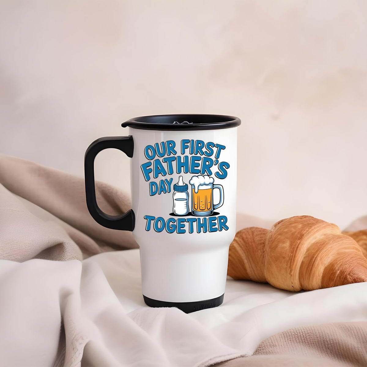 First Father’s Day bottle and beer travel mug on a soft blanket beside a croissant